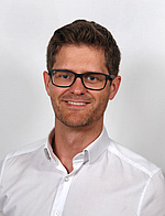 ein Mann mit kurzen braunen Haaren, einer Brille und weißem Hemd.